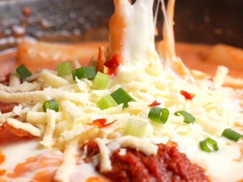 Close up of creamy rose tteokbokki with melted mozzarella and bacon in a skillet.