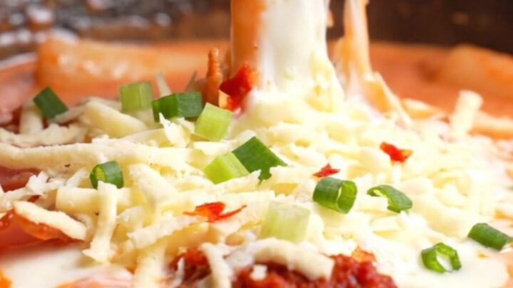 Close up of creamy rose tteokbokki with melted mozzarella and bacon in a skillet.
