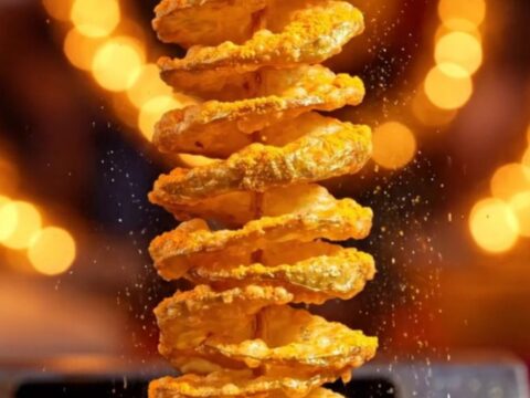 A golden, crispy tornado potato skewer seasoned with cheddar powder, glistening in the light.