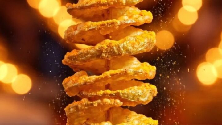A golden, crispy tornado potato skewer seasoned with cheddar powder, glistening in the light.