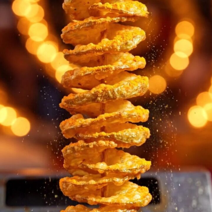 A golden, crispy tornado potato skewer seasoned with cheddar powder, glistening in the light.