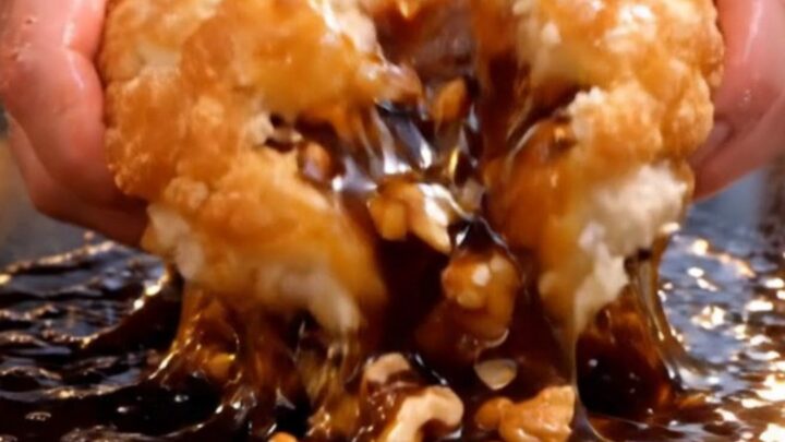 A close-up of a golden brown, crispy Korean hotteok pancake being torn open to reveal a molten cinnamon and nut syrup.