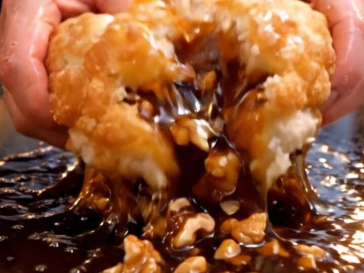 A close-up of a golden brown, crispy Korean hotteok pancake being torn open to reveal a molten cinnamon and nut syrup.