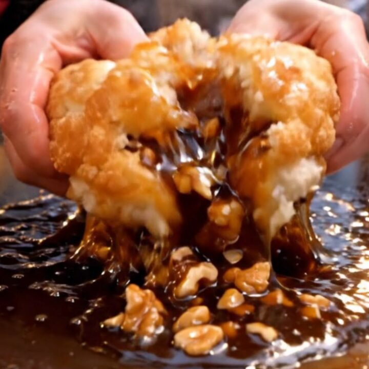 A close-up of a golden brown, crispy Korean hotteok pancake being torn open to reveal a molten cinnamon and nut syrup.