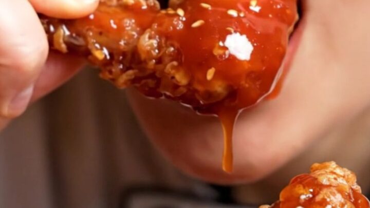 Close-up of double-fried Korean chicken wings glistening with a sticky red gochujang glaze and sesame seeds.