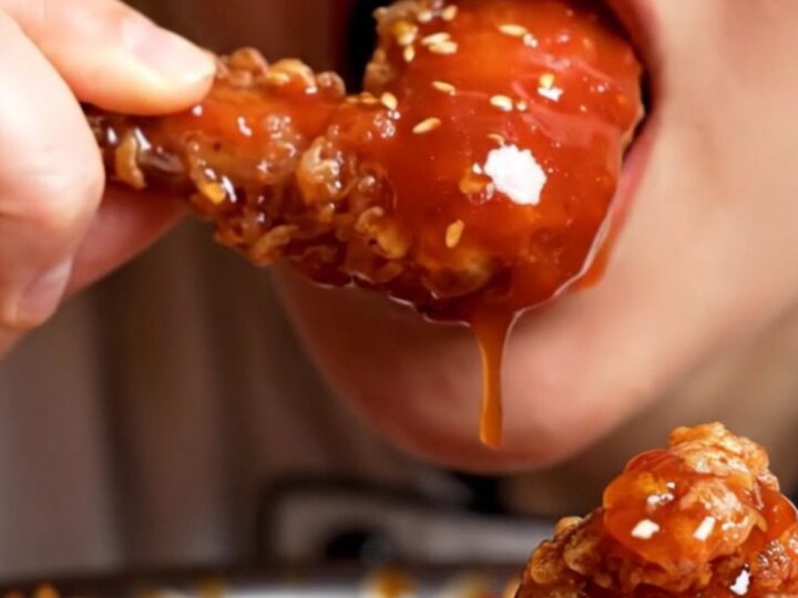Close-up of double-fried Korean chicken wings glistening with a sticky red gochujang glaze and sesame seeds.