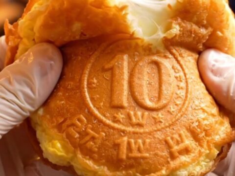 A golden, coin-shaped pancake split in half showing a long, stretchy pull of melted mozzarella cheese.