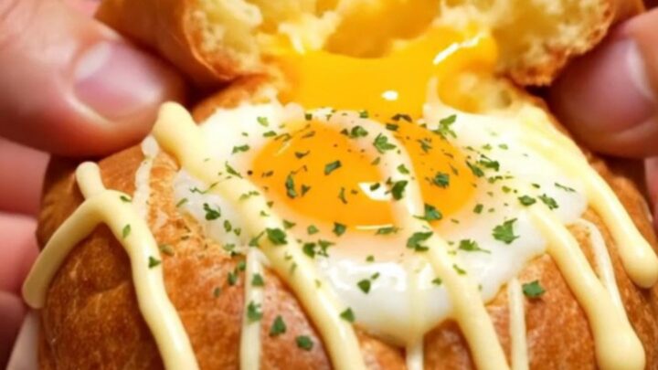 A macro shot of a fluffy, oval-shaped Korean egg bread broken in half, revealing a runny egg yolk, melted cheese, and bacon.
