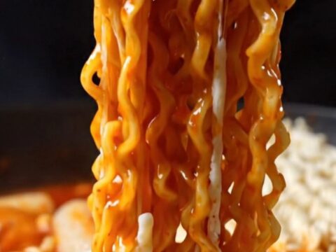 A steaming skillet of cheesy Korean rabokki with visible noodles and rice cakes covered in melted mozzarella.