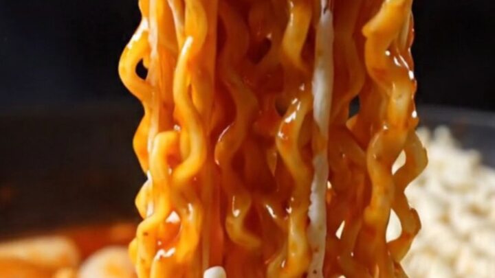 A steaming skillet of cheesy Korean rabokki with visible noodles and rice cakes covered in melted mozzarella.
