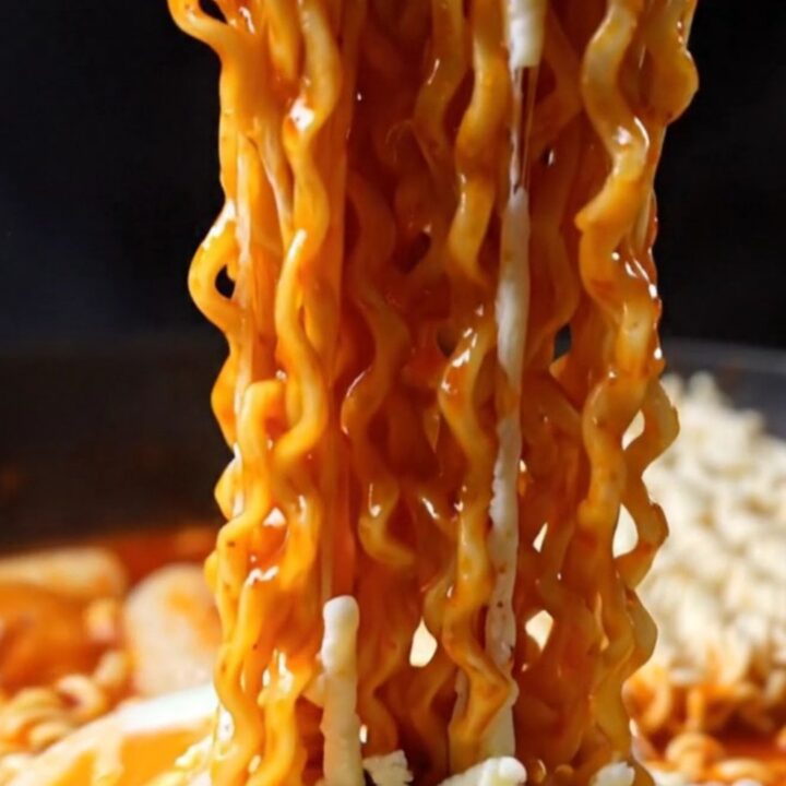 A steaming skillet of cheesy Korean rabokki with visible noodles and rice cakes covered in melted mozzarella.