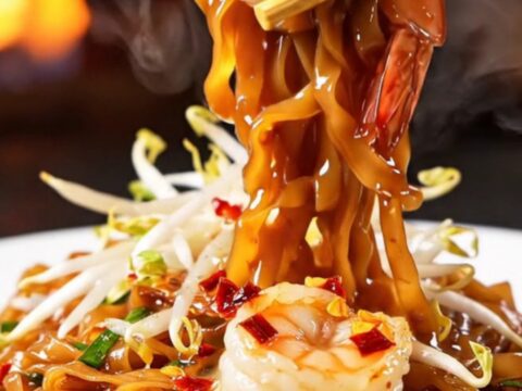A close-up of smoky Pad Thai with tiger prawns in a hot wok.