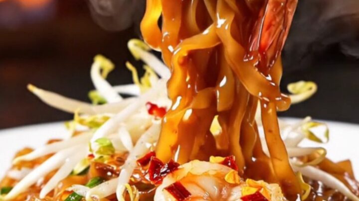 A close-up of smoky Pad Thai with tiger prawns in a hot wok.