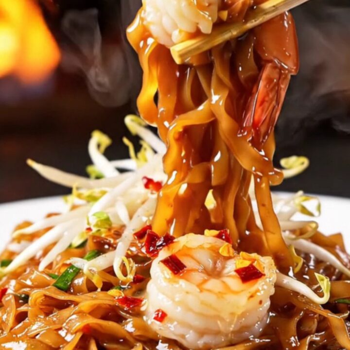 A close-up of smoky Pad Thai with tiger prawns in a hot wok.