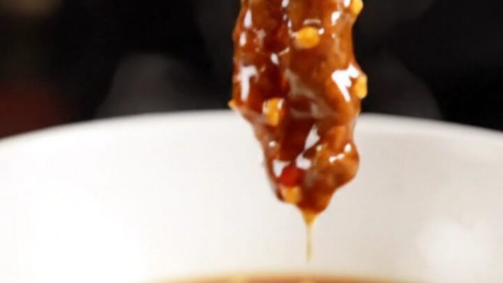 A close-up of crispy Beijing beef strips coated in a glossy, dark red garlic glaze with sliced red peppers.