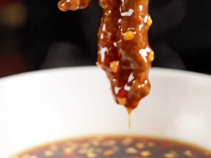 A close-up of crispy Beijing beef strips coated in a glossy, dark red garlic glaze with sliced red peppers.