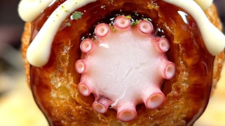 A close-up of golden, crispy takoyaki balls served on a plate with bonito flakes dancing on top.