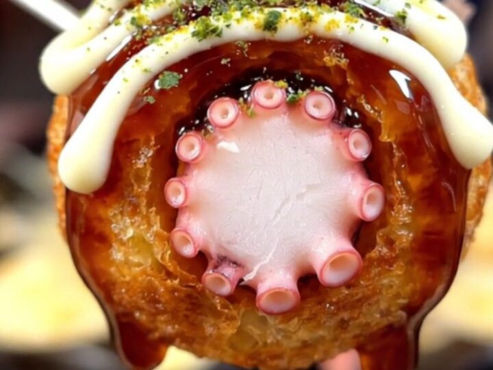 A close-up of golden, crispy takoyaki balls served on a plate with bonito flakes dancing on top.