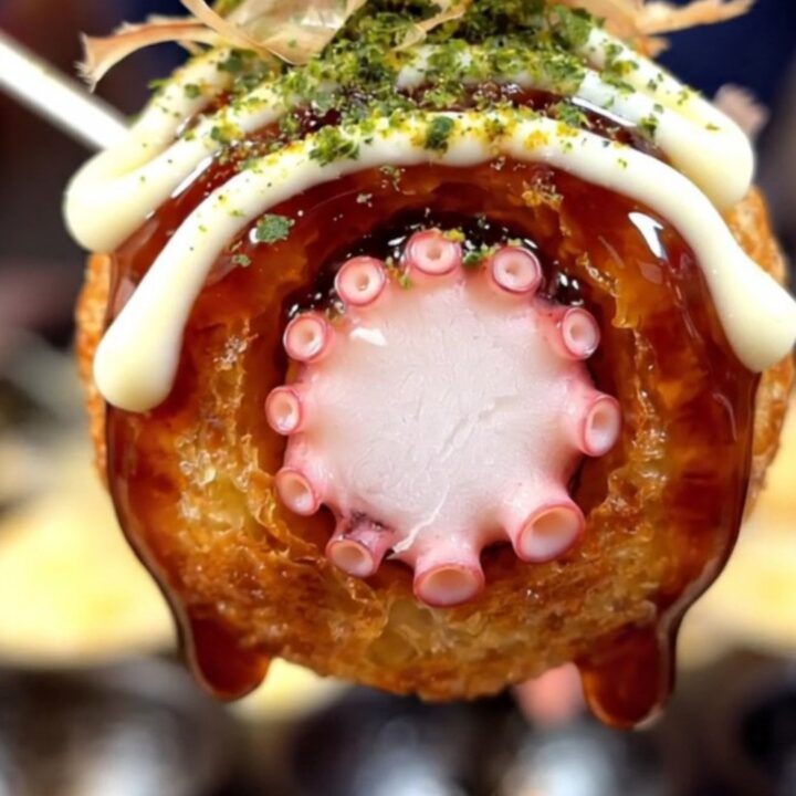 A close-up of golden, crispy takoyaki balls served on a plate with bonito flakes dancing on top.
