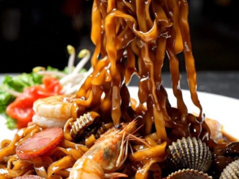 A close-up shot of smoky Penang Char Kway Teow with charred noodles, plump prawns, and sliced lap cheong sausage.
