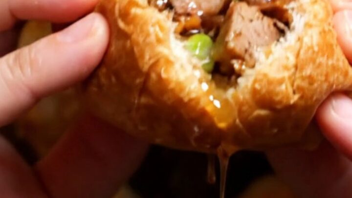 A close-up of a crispy Taiwanese black pepper pork bun broken in half, revealing juicy pork and green scallions.