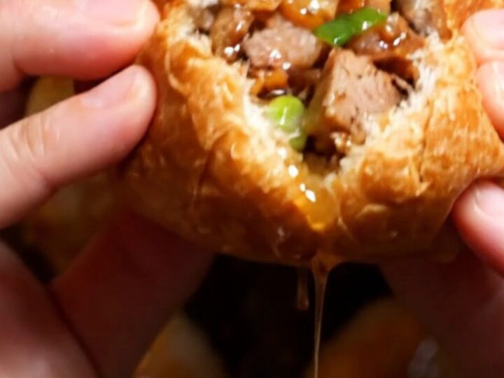 A close-up of a crispy Taiwanese black pepper pork bun broken in half, revealing juicy pork and green scallions.
