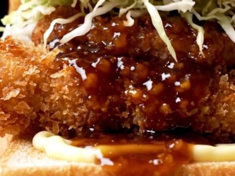 A close-up view of a crispy chicken katsu sando on shokupan bread, showcasing the golden panko crust and fresh cabbage.