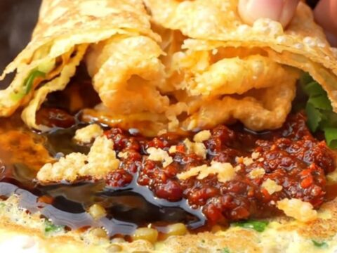 A warm Beijing-style jianbing crepe folded around a crispy wonton cracker, garnished with cilantro and scallions.