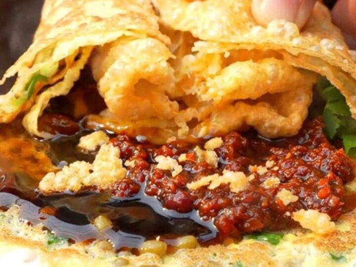 A warm Beijing-style jianbing crepe folded around a crispy wonton cracker, garnished with cilantro and scallions.