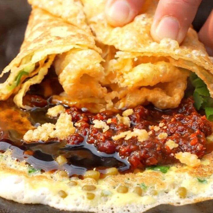 A warm Beijing-style jianbing crepe folded around a crispy wonton cracker, garnished with cilantro and scallions.