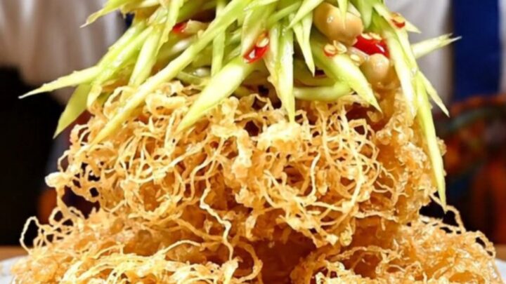 A crispy, golden nest of fried catfish topped with vibrant green mango salad, red chilies, and fresh herbs.