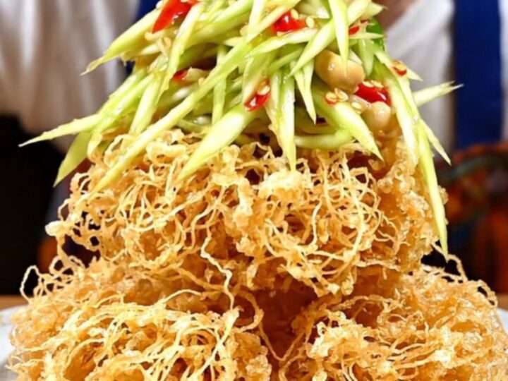 A crispy, golden nest of fried catfish topped with vibrant green mango salad, red chilies, and fresh herbs.