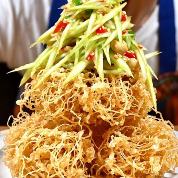 A crispy, golden nest of fried catfish topped with vibrant green mango salad, red chilies, and fresh herbs.