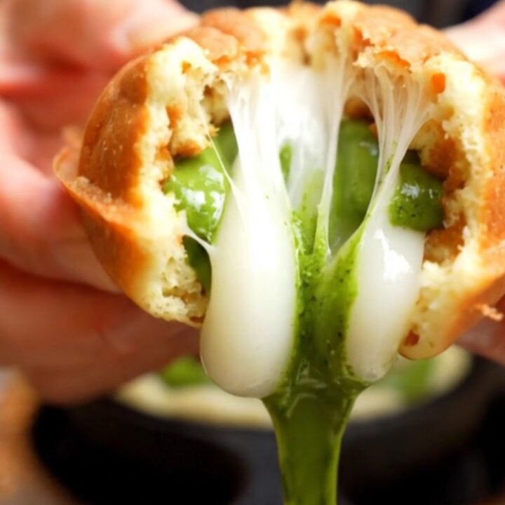 A crisp, golden-brown fish-shaped taiyaki waffle being pulled apart to reveal a vibrant green matcha custard and stretchy