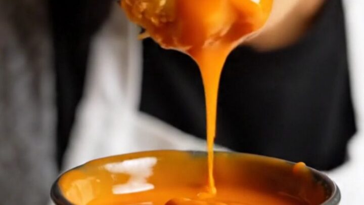 A close-up of crispy, golden-brown cauliflower florets tossed in a glossy, fiery orange Bang Bang sauce.