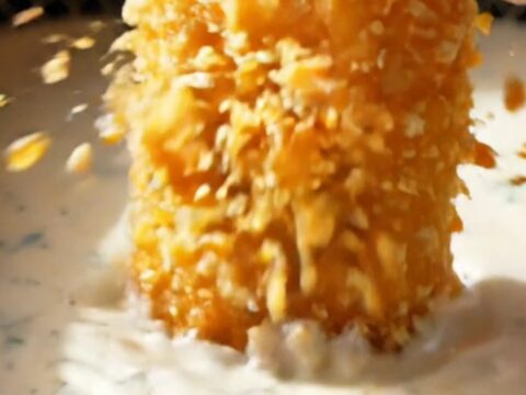 A close-up of a crispy air-fryer dill pickle chip being held between fingers, showing the golden panko crust.