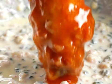 A close-up of a crispy buffalo cauliflower wing being dipped into a bowl of creamy blue cheese dressing.