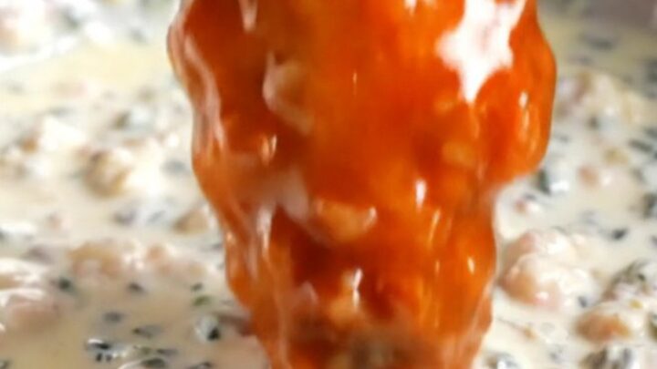 A close-up of a crispy buffalo cauliflower wing being dipped into a bowl of creamy blue cheese dressing.
