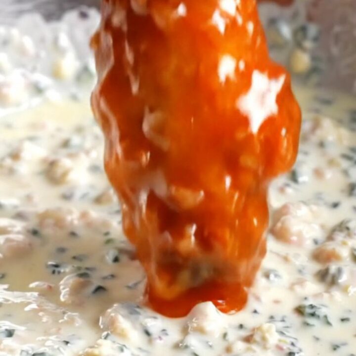 A close-up of a crispy buffalo cauliflower wing being dipped into a bowl of creamy blue cheese dressing.