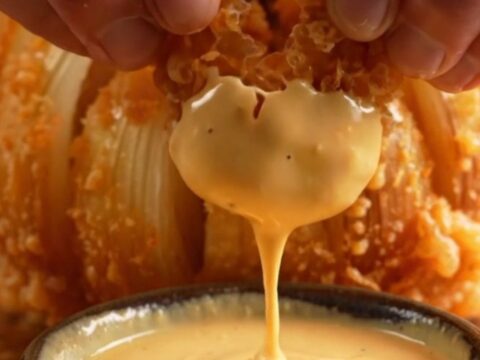 A golden, crispy blooming onion sitting on a plate with a side of creamy orange comeback sauce.