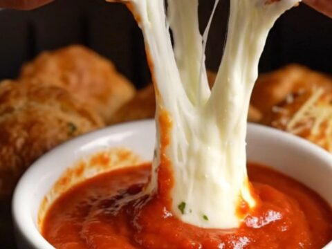 A close-up of a golden air-fried bread bomb pulled apart, showing a long, stretchy mozzarella cheese bridge.