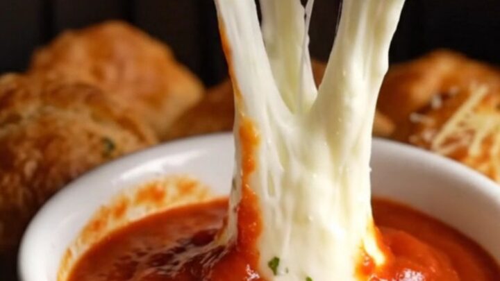 A close-up of a golden air-fried bread bomb pulled apart, showing a long, stretchy mozzarella cheese bridge.