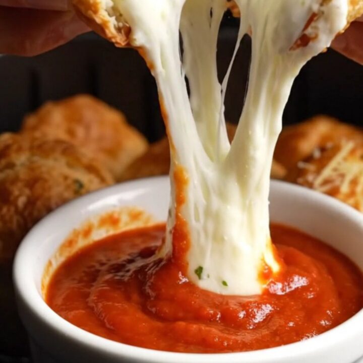 A close-up of a golden air-fried bread bomb pulled apart, showing a long, stretchy mozzarella cheese bridge.
