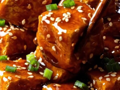 A close-up shot of golden, crispy air-fried tofu chunks coated in a glossy, dark General Tso's glaze