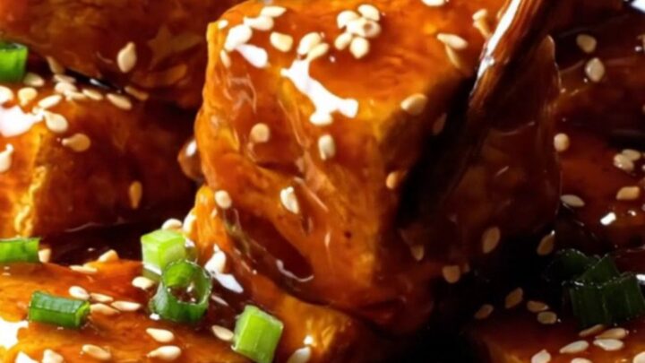 A close-up shot of golden, crispy air-fried tofu chunks coated in a glossy, dark General Tso's glaze