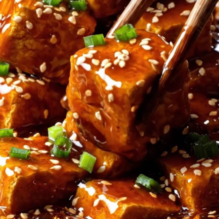 A close-up shot of golden, crispy air-fried tofu chunks coated in a glossy, dark General Tso's glaze