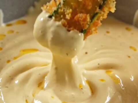 A close-up of golden, crispy air-fryer zucchini fries stacked neatly next to a bowl of creamy lemon-garlic aioli.