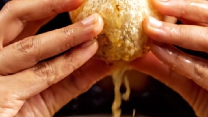 A close-up shot of a crispy, golden pani puri sphere filled with a savory potato and chickpea mix, ready for a bite.