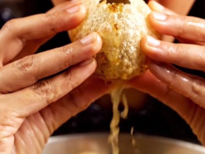 A close-up shot of a crispy, golden pani puri sphere filled with a savory potato and chickpea mix, ready for a bite.