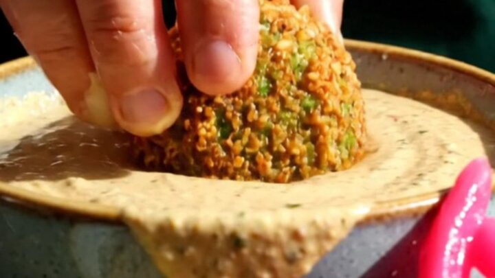 A close-up of a crispy, golden-brown falafel ball broken open to reveal a vibrant, emerald-green herb interior.